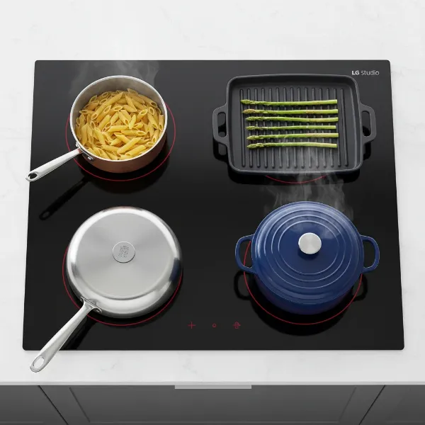 Various types of cookware on an induction cooktop, with a magnet demonstrating compatibility for one pot.